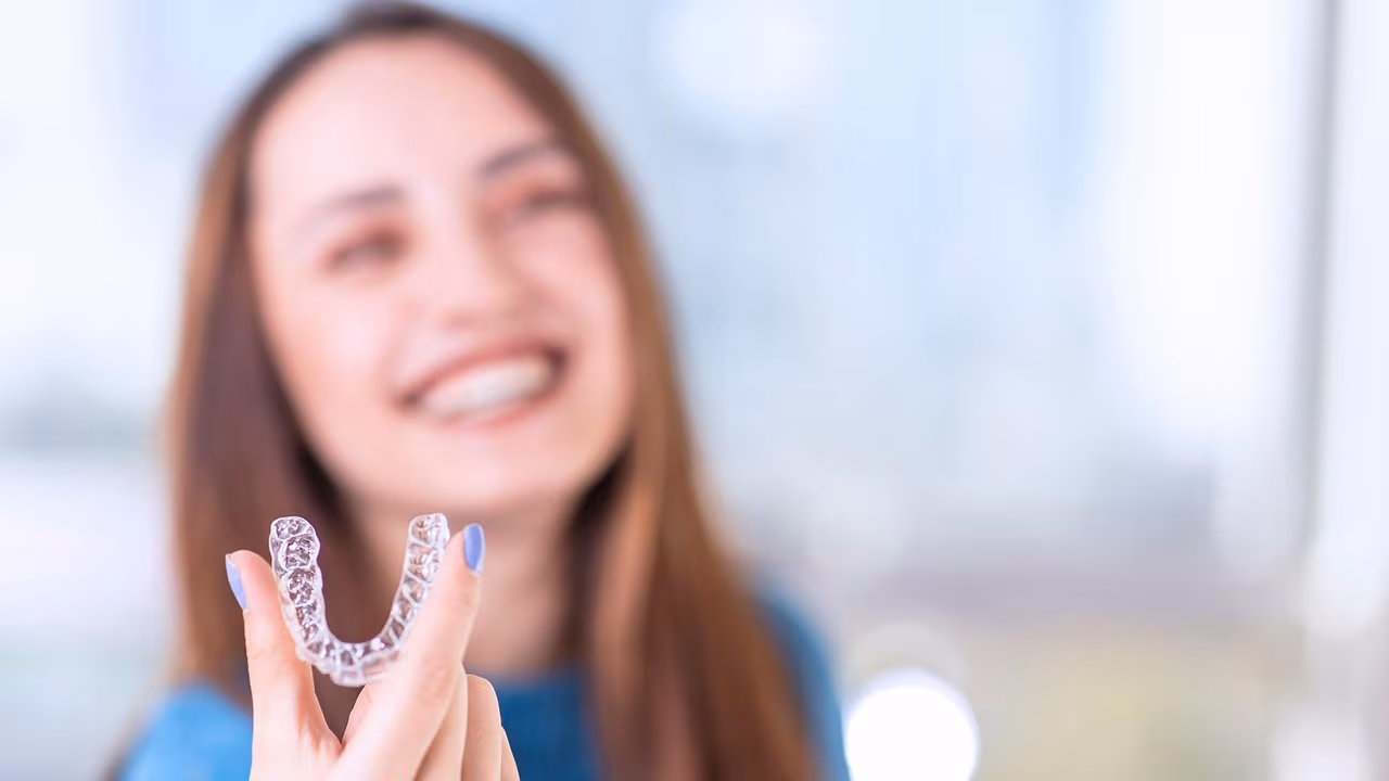 A patient holding a clear, nearly invisible Invisalign aligner tray